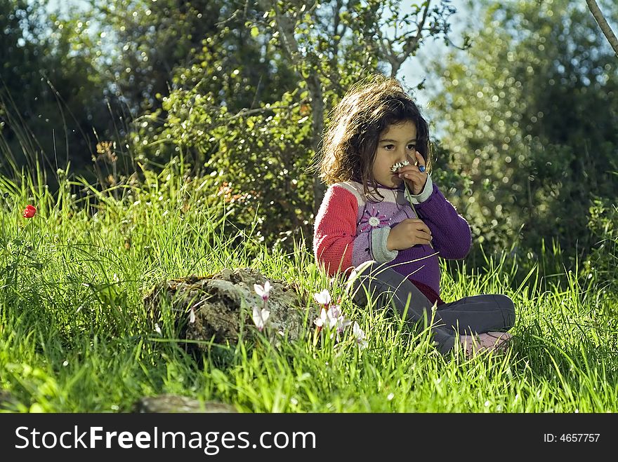 Girl sitting in grass smelling a flower