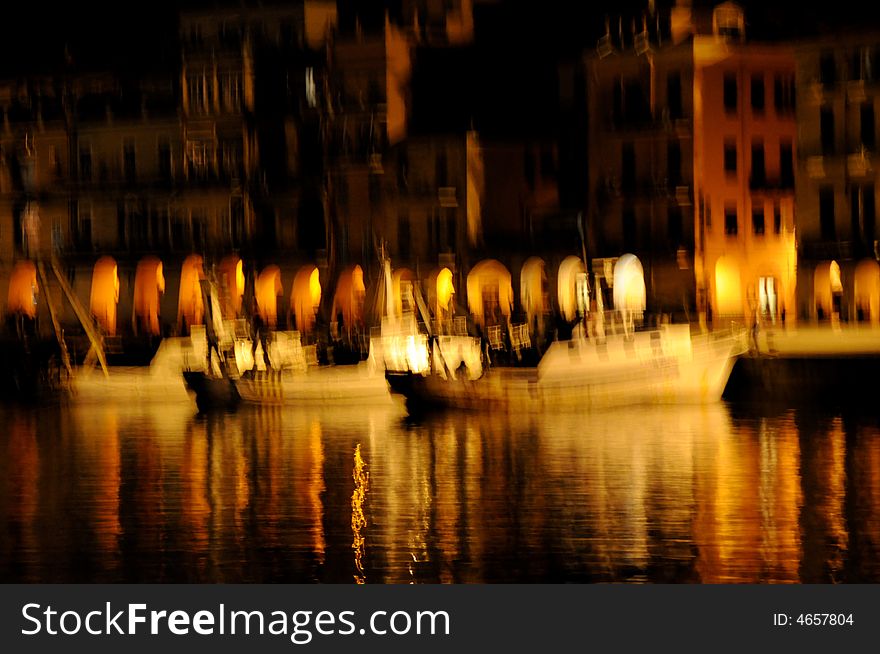 Three fishing boats are moored in the harbour of Imperia, Liguria, Italy, in a winter ending night. The hot lights on the dock illuminate boats and water here around. On the background the home and the portico illuminated. The blur effect gives to the image an oil painted looking. Three fishing boats are moored in the harbour of Imperia, Liguria, Italy, in a winter ending night. The hot lights on the dock illuminate boats and water here around. On the background the home and the portico illuminated. The blur effect gives to the image an oil painted looking