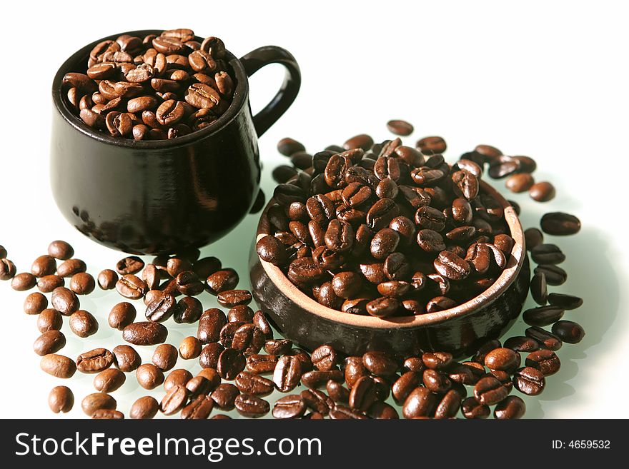 Coffee beans of two kind in a little brown cup and saucer on a white background. Coffee beans of two kind in a little brown cup and saucer on a white background