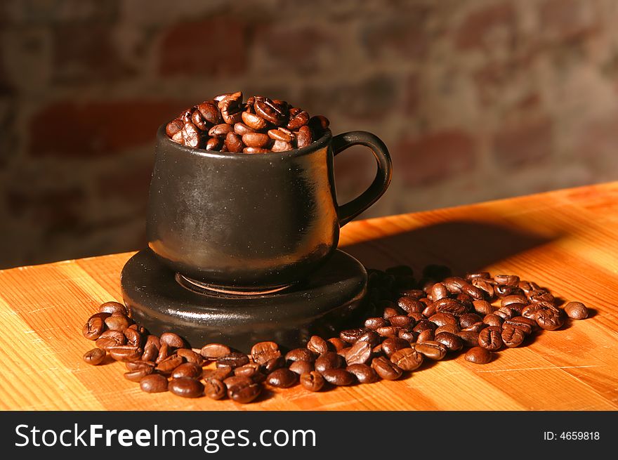 Little brown cup and spilled out coffee beans on soft focus background on wood table. Little brown cup and spilled out coffee beans on soft focus background on wood table