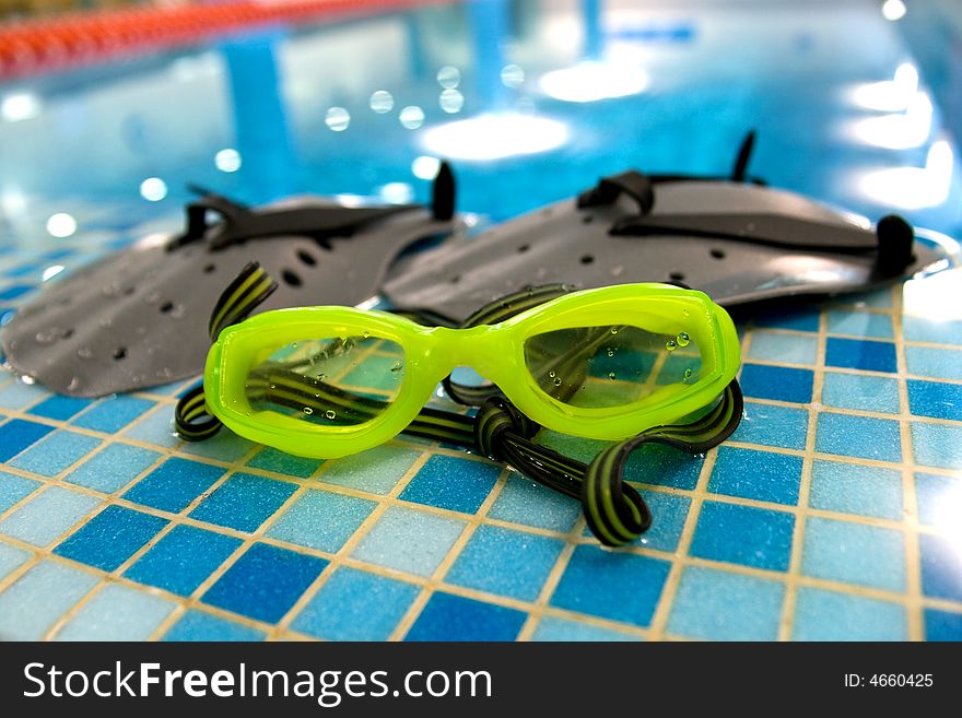 Glasses and paddle for swim lay on the coast of swimming pool. Glasses and paddle for swim lay on the coast of swimming pool