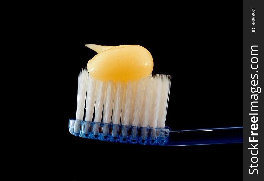 Yellow toothpaste on toothbrush and a black background