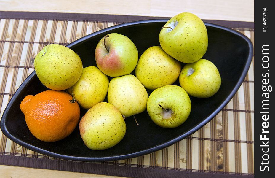 Black Japanese vase with apples and tangerine served at wooden table