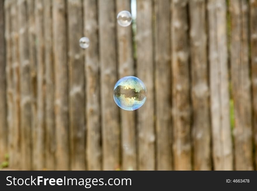 Flying soap bubbles reflecting wooden fence on the background