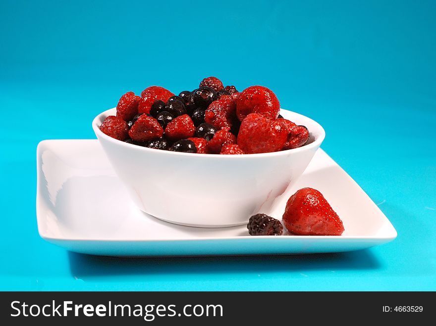 White bowl of mixed berries with blue background. White bowl of mixed berries with blue background.