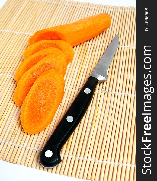 Carrot sliced , knife behind the carrot, and a bamboo carpet background.