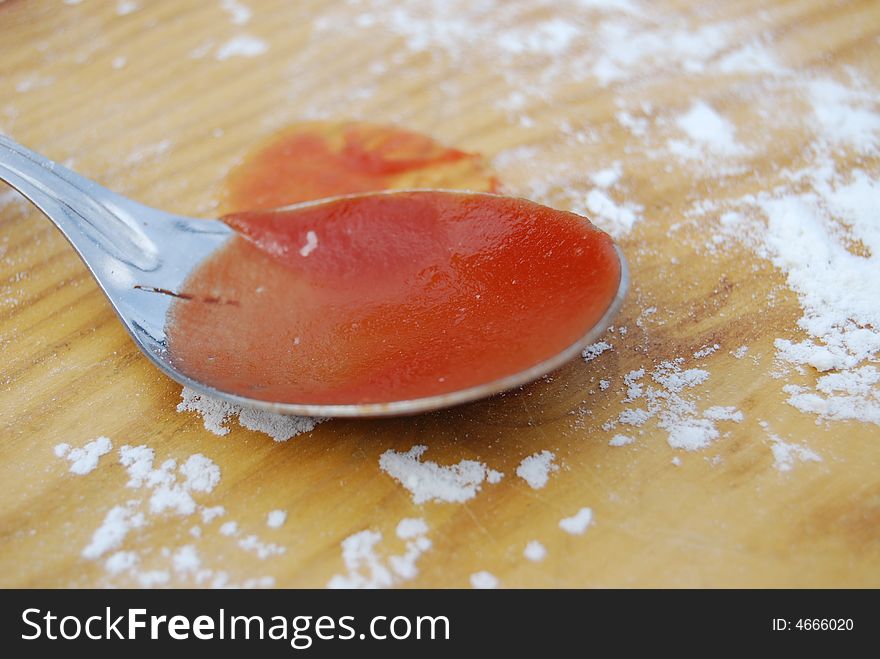 A spoon with red tomato sauce and flour on a wooden table