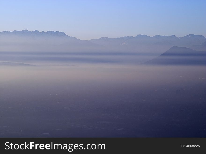 The city of Turin, Piedmont, Italy, lies hidden by dense smog and mist on a late winter afternoon. The peaks of the alps can be seen emrging from the mist in the background. The city of Turin, Piedmont, Italy, lies hidden by dense smog and mist on a late winter afternoon. The peaks of the alps can be seen emrging from the mist in the background.