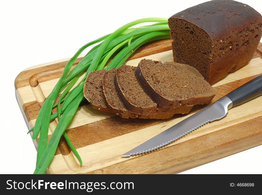 Loaf of sliced grain bread with spring onions on wood bread board with knife isolated on white