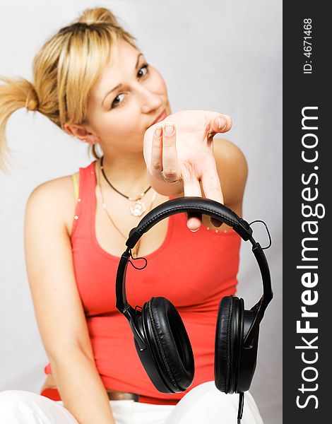 Sitting woman clothed in T-shirt and trousers holding headphones. Focus on headphones.