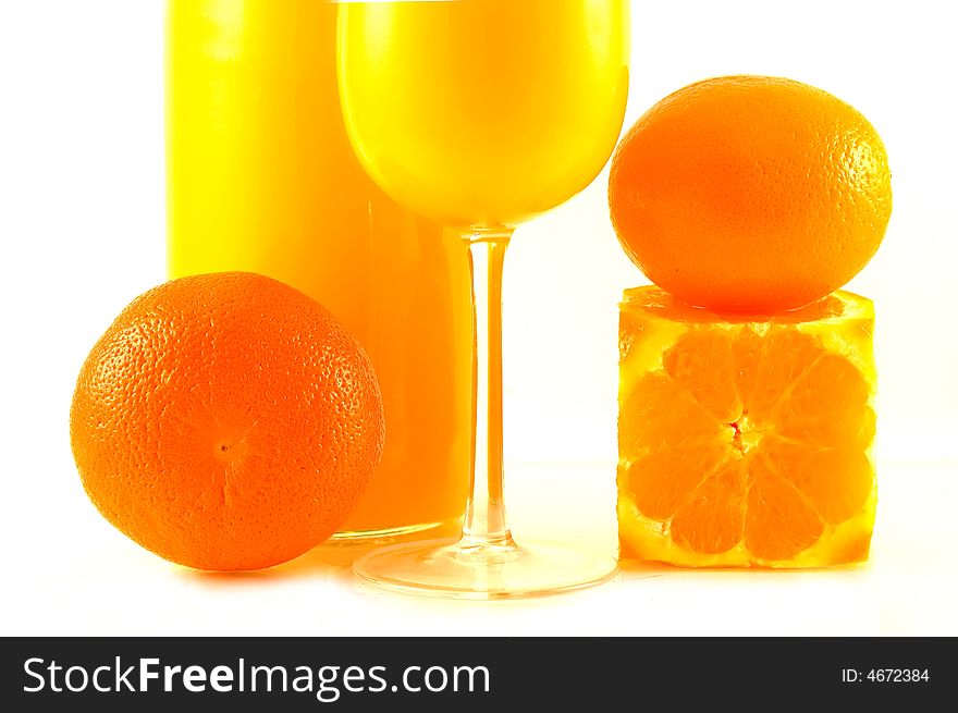 Partial view at the brightly lit oranges, bottle and glass with orange juice. Partial view at the brightly lit oranges, bottle and glass with orange juice