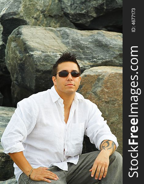 Man sitting on a rock with rocks as a background and wearing sunglasses. Man sitting on a rock with rocks as a background and wearing sunglasses