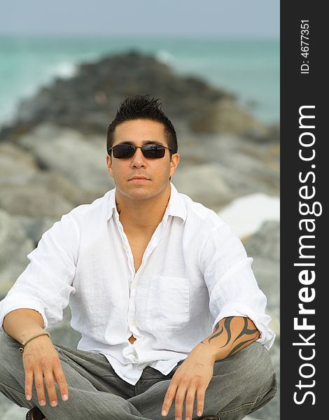 Young man with sunglasses sitting on rocks. Young man with sunglasses sitting on rocks