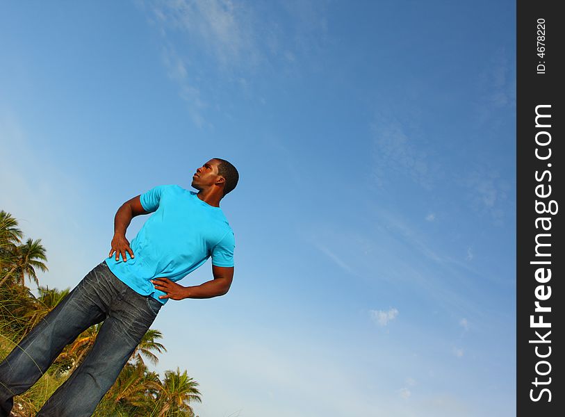 Young black man standing tall at an angle with a blue sky background behind him.