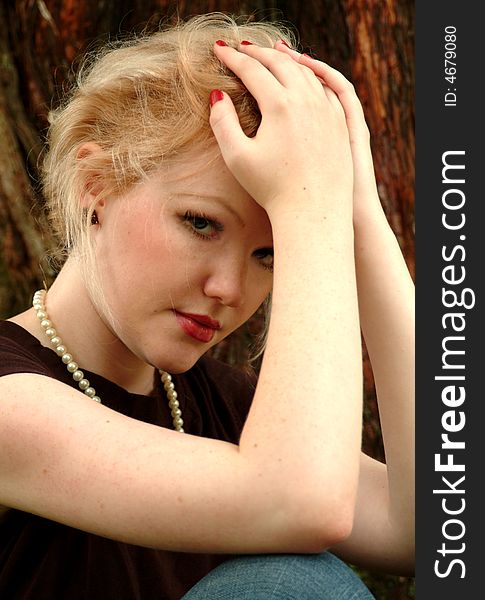 Young blond woman sitting beside cedar tree. Young blond woman sitting beside cedar tree