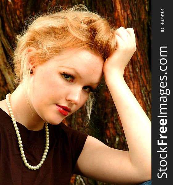 Young blond woman sitting beside cedar tree. Young blond woman sitting beside cedar tree