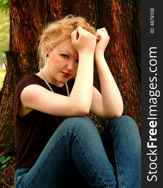 Young blond woman sitting beside cedar tree. Young blond woman sitting beside cedar tree