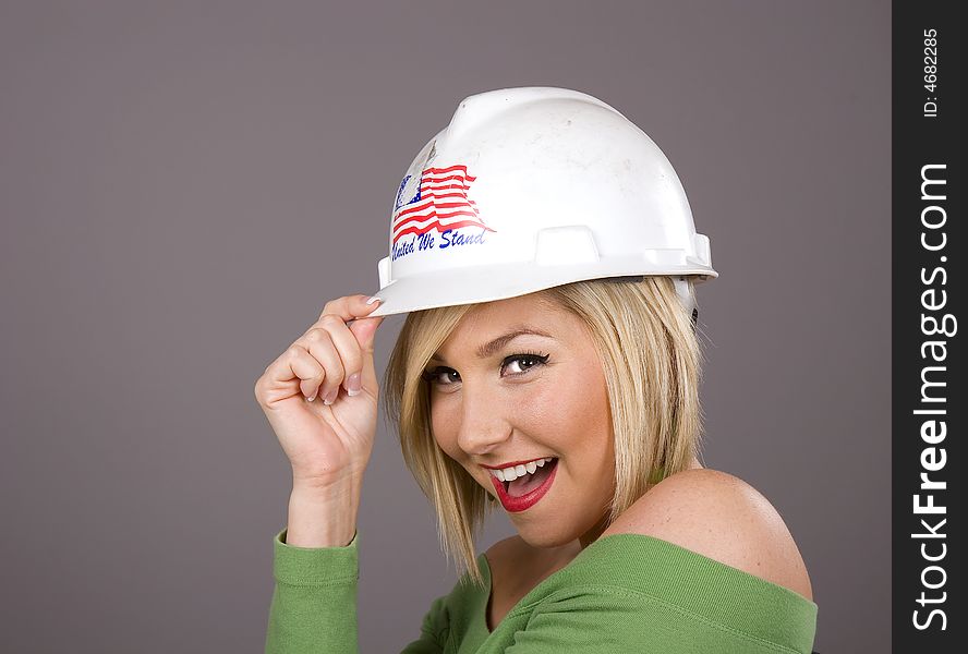 A blonde in a green blouse tipping a hard hat to the camera. A blonde in a green blouse tipping a hard hat to the camera