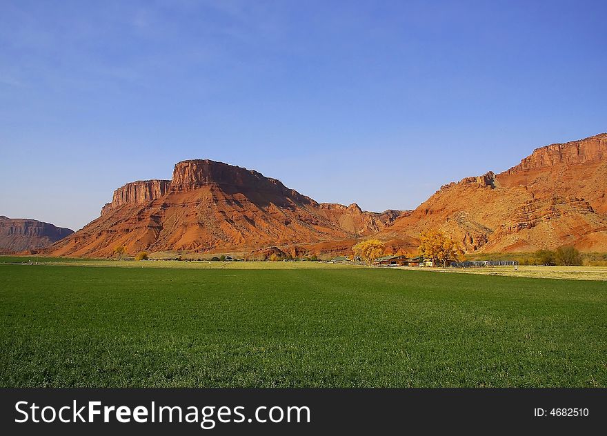 View of a farm in the desert with hay in the foreground and a red rock mountain in the background with blue skyï¿½s and puffy clouds. View of a farm in the desert with hay in the foreground and a red rock mountain in the background with blue skyï¿½s and puffy clouds