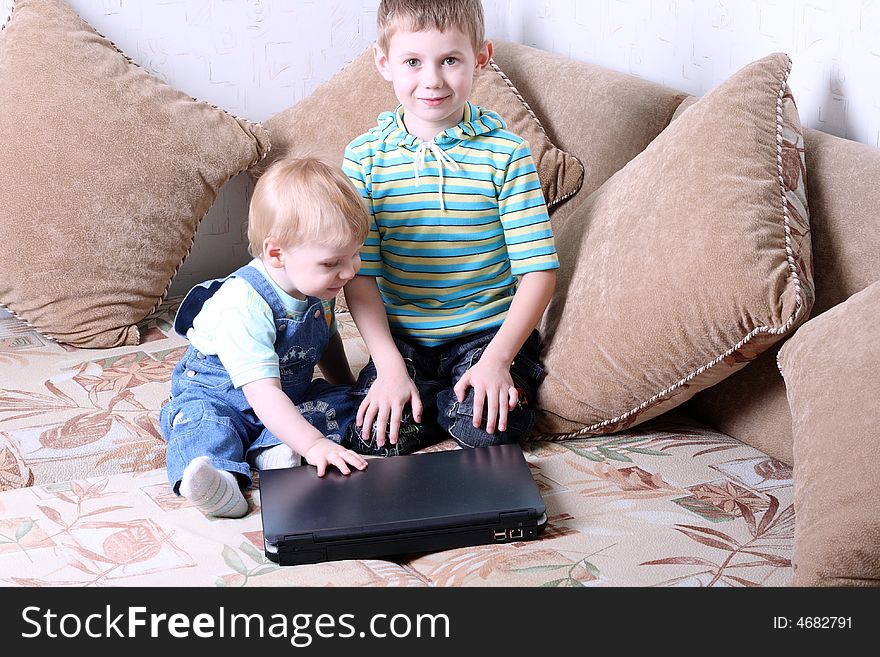 Two small boys together play near a laptop. Two small boys together play near a laptop