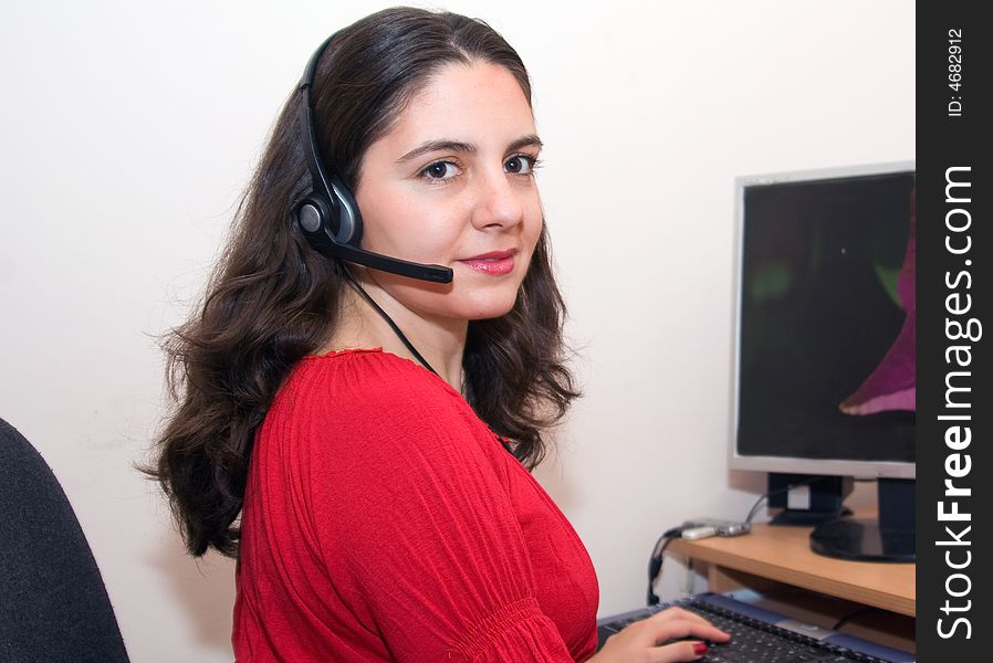 A girl, sitting at her desktop, wearing headphones and microphone, looking tenderly. A girl, sitting at her desktop, wearing headphones and microphone, looking tenderly