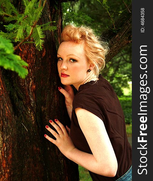 Young blond woman leaning on cedar tree