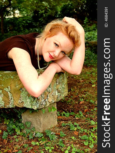 Young blond woman lying on old stone bench, looking at camera. Young blond woman lying on old stone bench, looking at camera