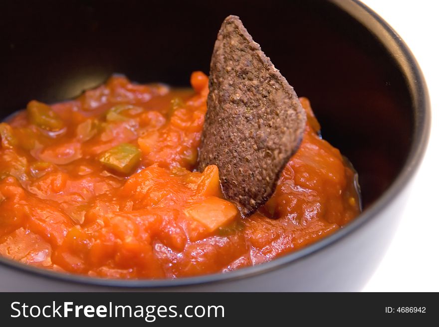 A blue corn chip in a bowl of red salsa. A blue corn chip in a bowl of red salsa.