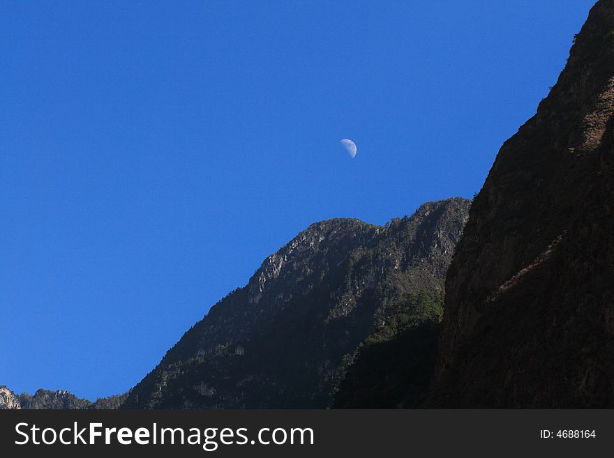 The moon above the mountains in the blue sky