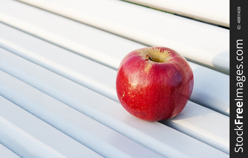 Bright red apple on the bench outside