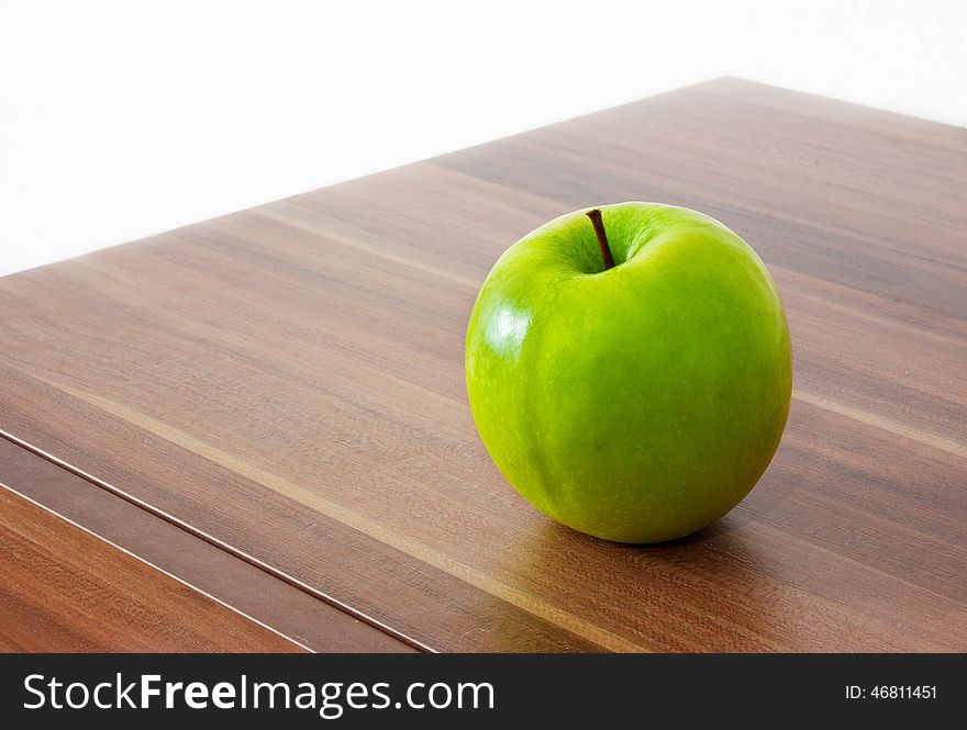 One green apple on the brown wooden table. One green apple on the brown wooden table