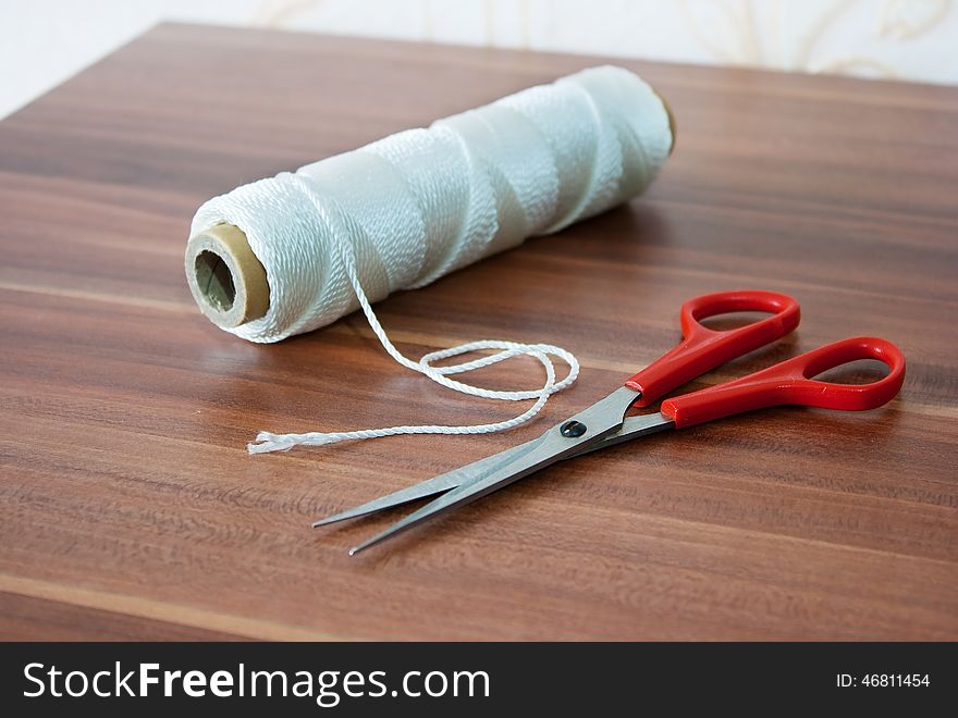 Spool of white thread and scissors on the table. Spool of white thread and scissors on the table