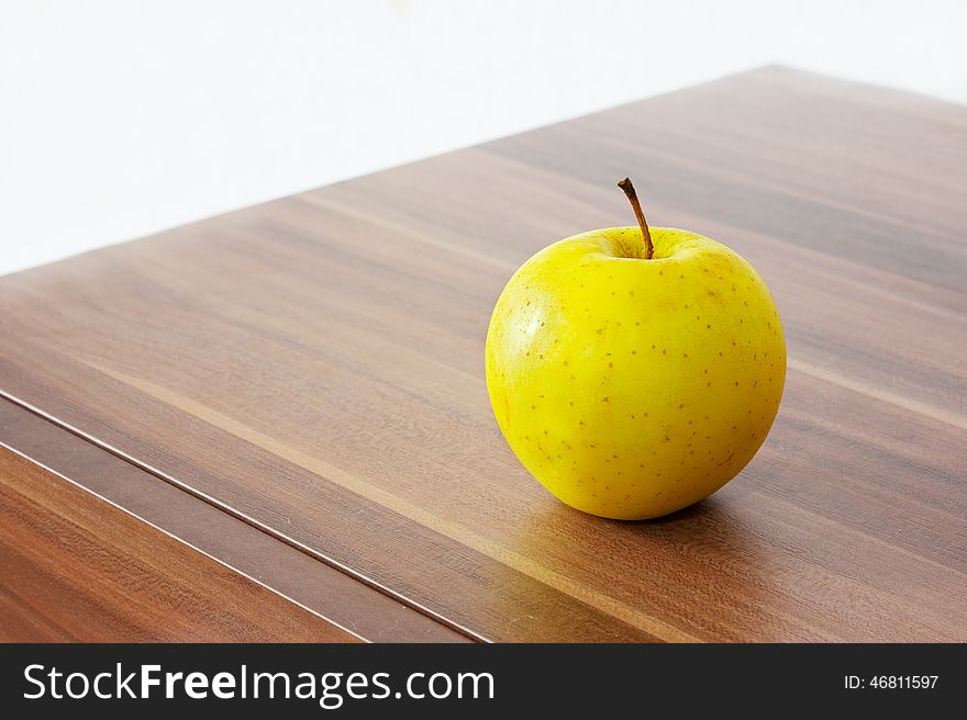 One yellow apple on the brown wooden table