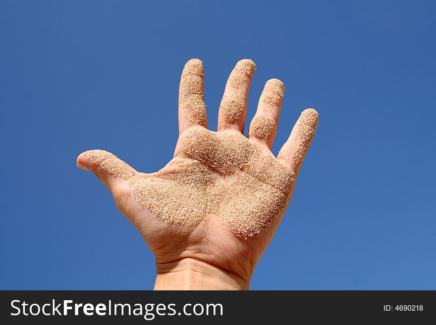 Woman's hand with sand on blue sky. Woman's hand with sand on blue sky