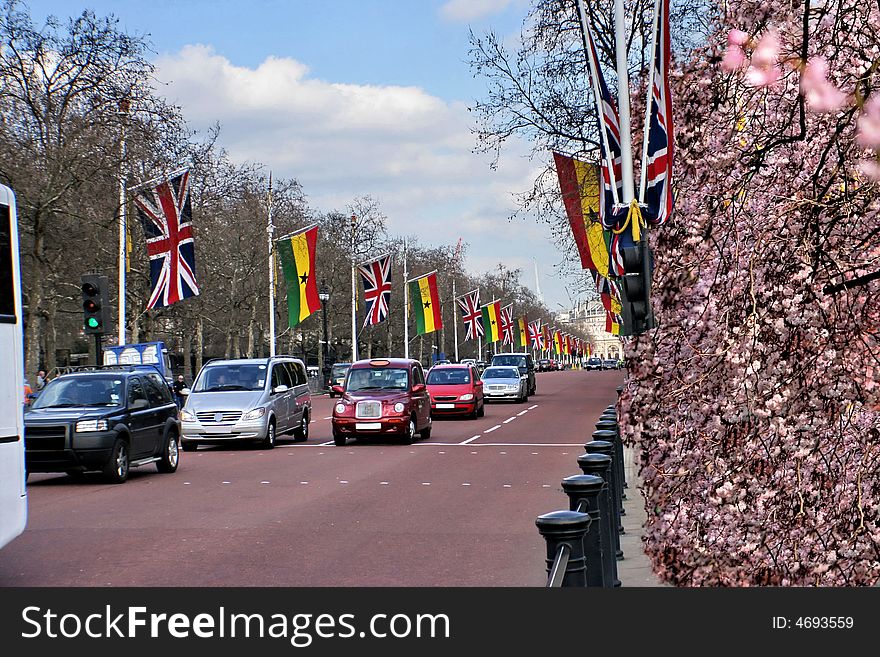 There are cars are on Buckingham palace  and surrounded by colorful flags and flowers. . There are cars are on Buckingham palace  and surrounded by colorful flags and flowers.