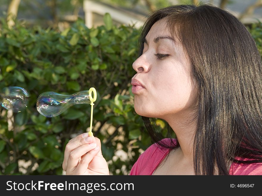 A pretty young woman blowing elongated bubbles from a wand. A pretty young woman blowing elongated bubbles from a wand.