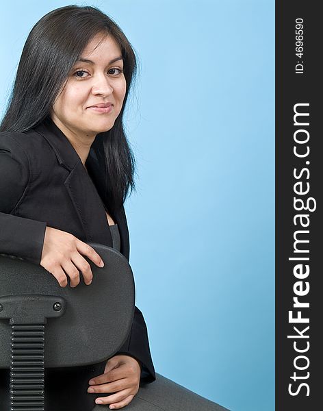 A pretty confident young woman sitting in an office chair, taken against a blue background. A pretty confident young woman sitting in an office chair, taken against a blue background.