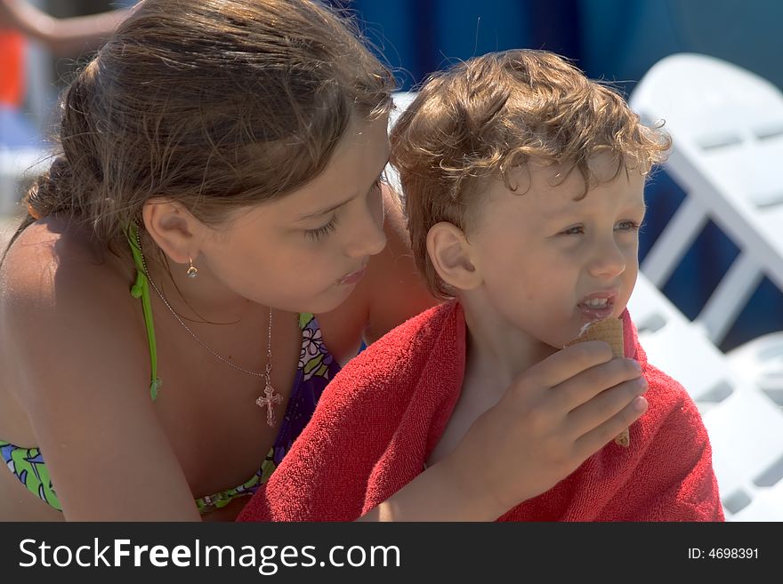 The white girl-teenager feeds the younger brother dressed in a red terry towel by ice-cream. The white girl-teenager feeds the younger brother dressed in a red terry towel by ice-cream