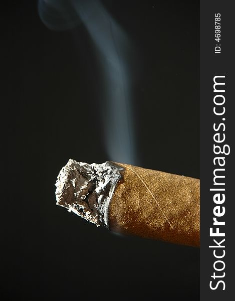 A smoking, cigar with ashes on a dark background. A smoking, cigar with ashes on a dark background