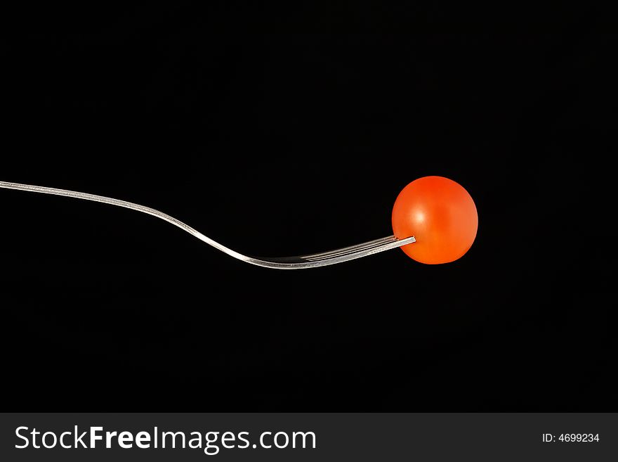 A red tomato on a fork against a black background