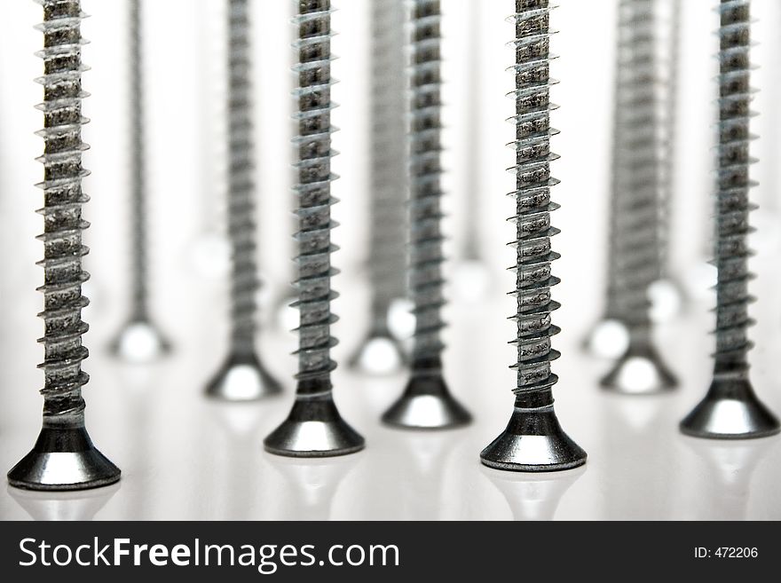 Bunch of screws standing on a white reflective background. Bunch of screws standing on a white reflective background.