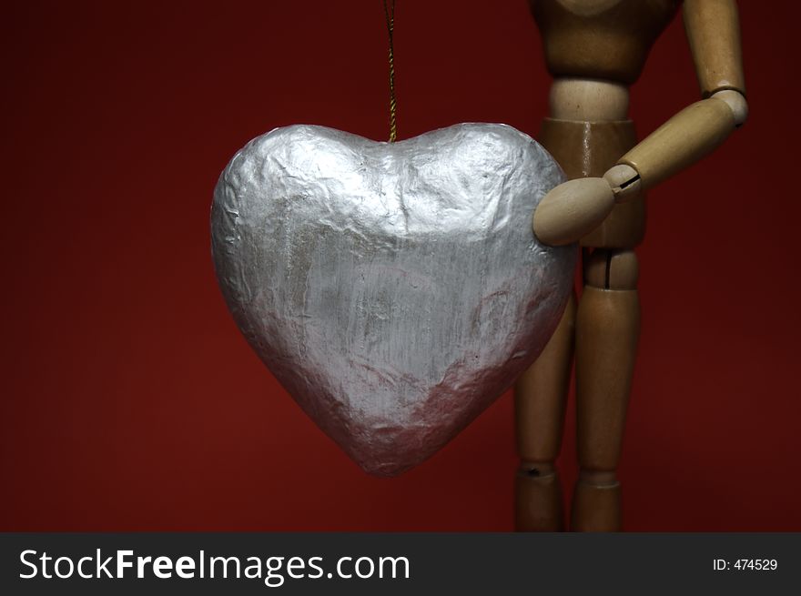 A manikin holds up a large silver heart against a deep red background. A manikin holds up a large silver heart against a deep red background.