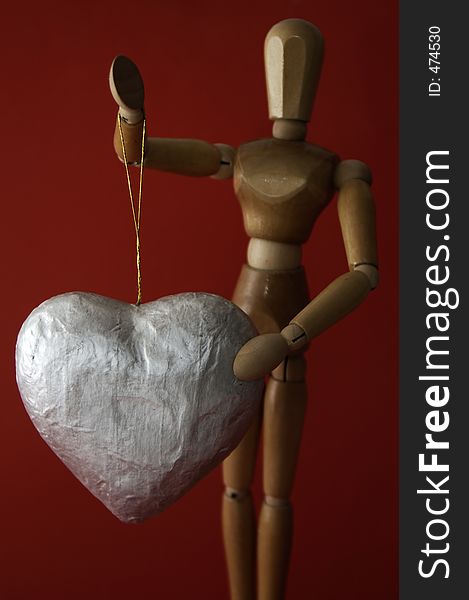 A manikin holds up a large silver heart on a string against a rich red background. A manikin holds up a large silver heart on a string against a rich red background.