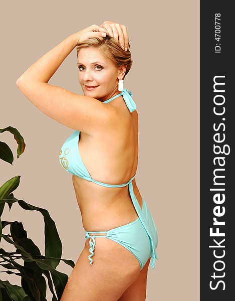 An friendly blond girl in a turquoise bikini standing in an studio whit a big plant
for white background. An friendly blond girl in a turquoise bikini standing in an studio whit a big plant
for white background.