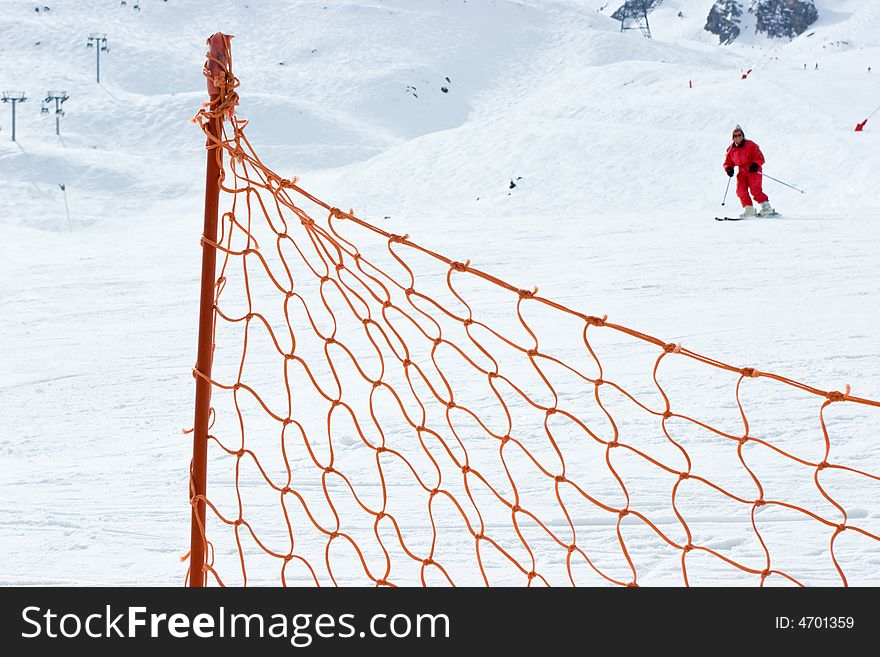 Red fence at ski slope with moving skier at background. Red fence at ski slope with moving skier at background