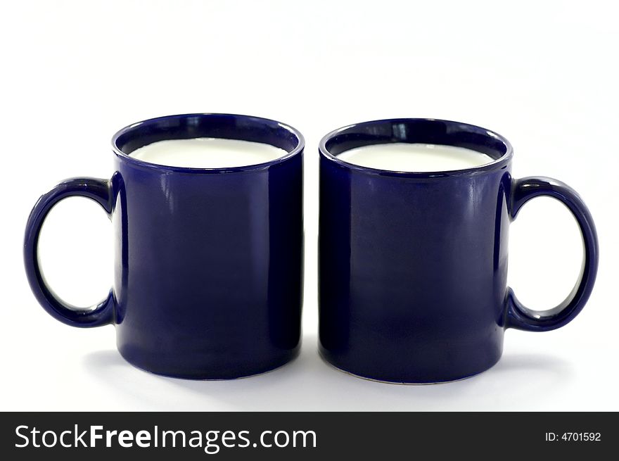 Two dark-blue cups with the milk against the white background