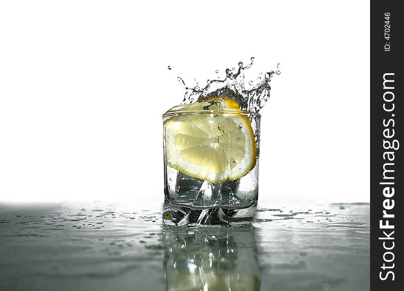 Glass of cold clear splashing water with falling lemon's slice on light-blue background. Glass of cold clear splashing water with falling lemon's slice on light-blue background