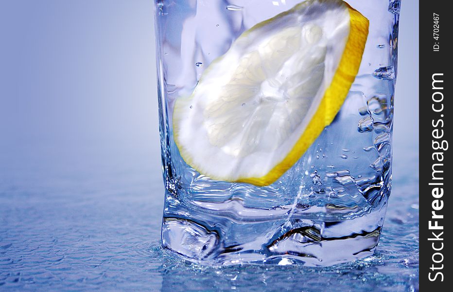 Glass of cold clear water with lemon's slice on light-blue background. Glass of cold clear water with lemon's slice on light-blue background