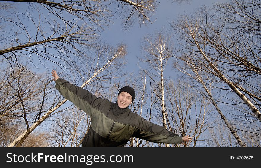 Young emotional guy has widely placed hands on background of trees. Young emotional guy has widely placed hands on background of trees