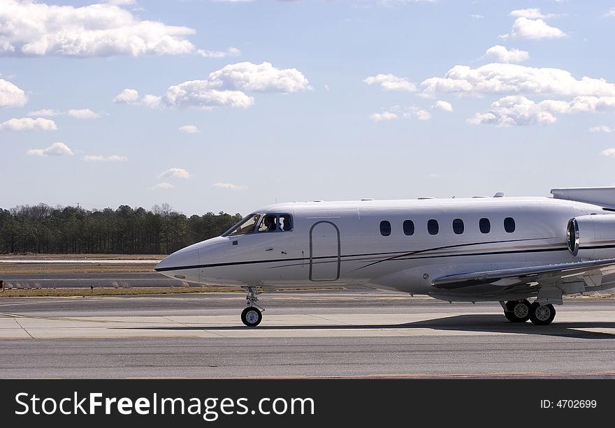 A large private jet taxiing on a runway under a sunny sky with clouds. A large private jet taxiing on a runway under a sunny sky with clouds